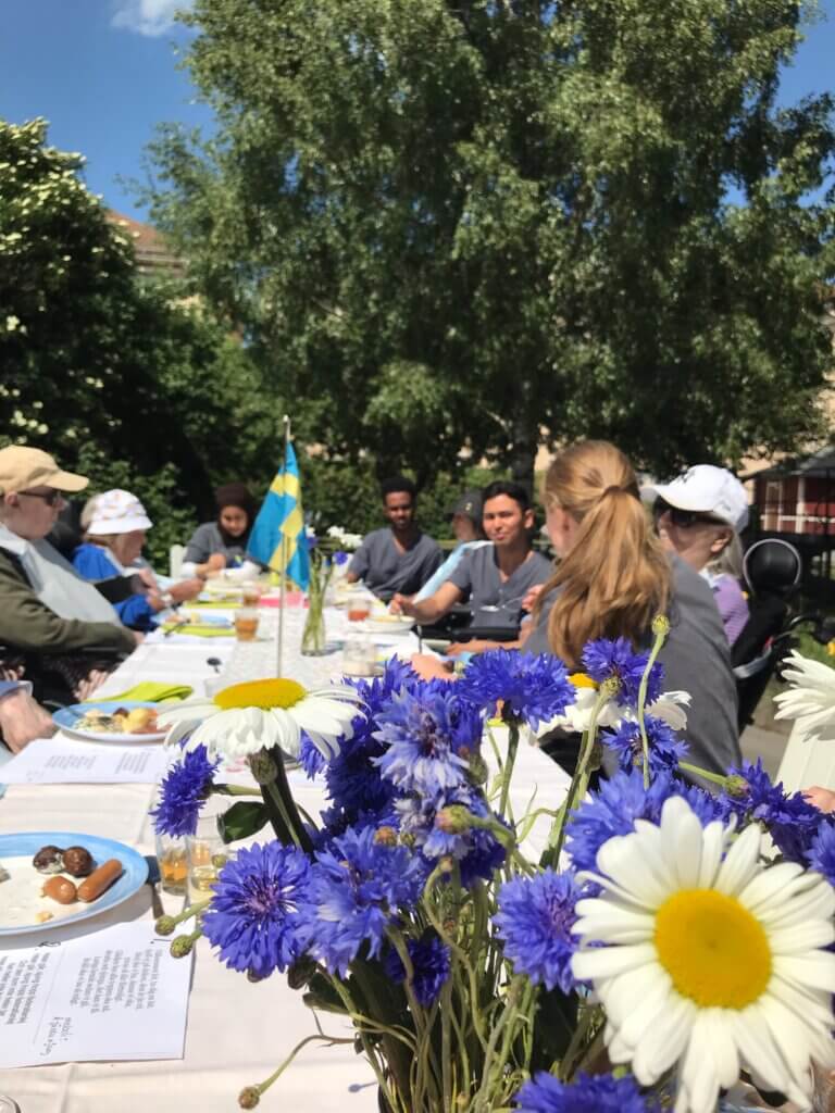 MIdsommarens sillunch vid långbord i trädgården, med blåklint och prästkragar på bordet.